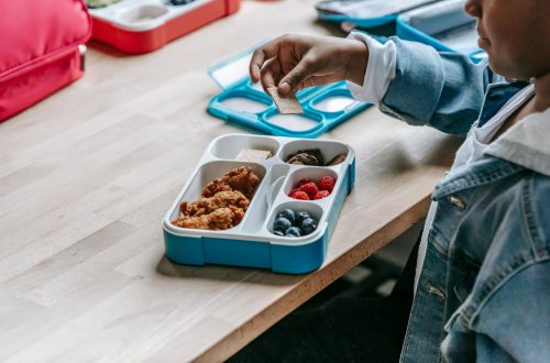 crop black schoolchild with biscuit near lunch box