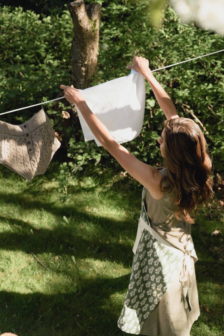 a woman hanging a white cloth on a clothes line