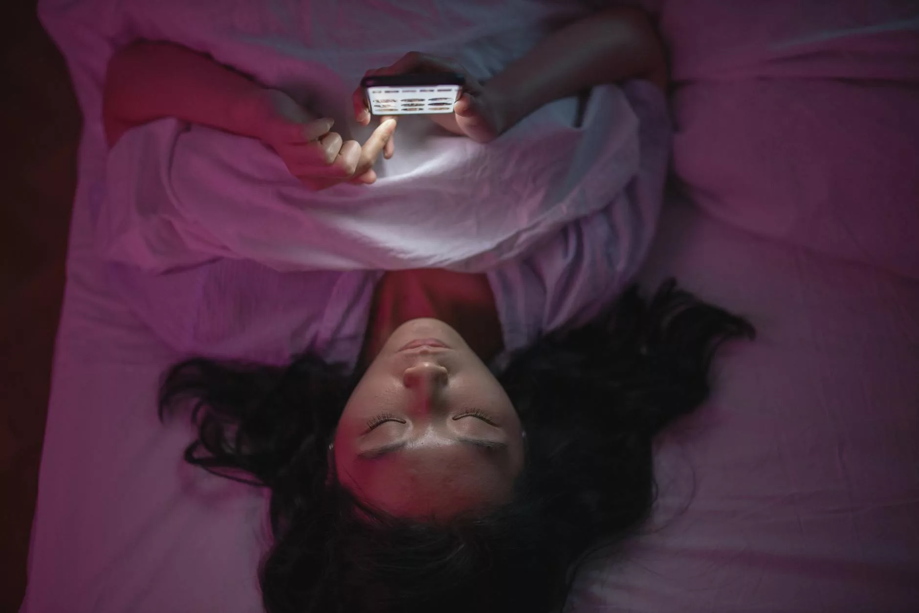 a woman lying on bed and holding an iphone