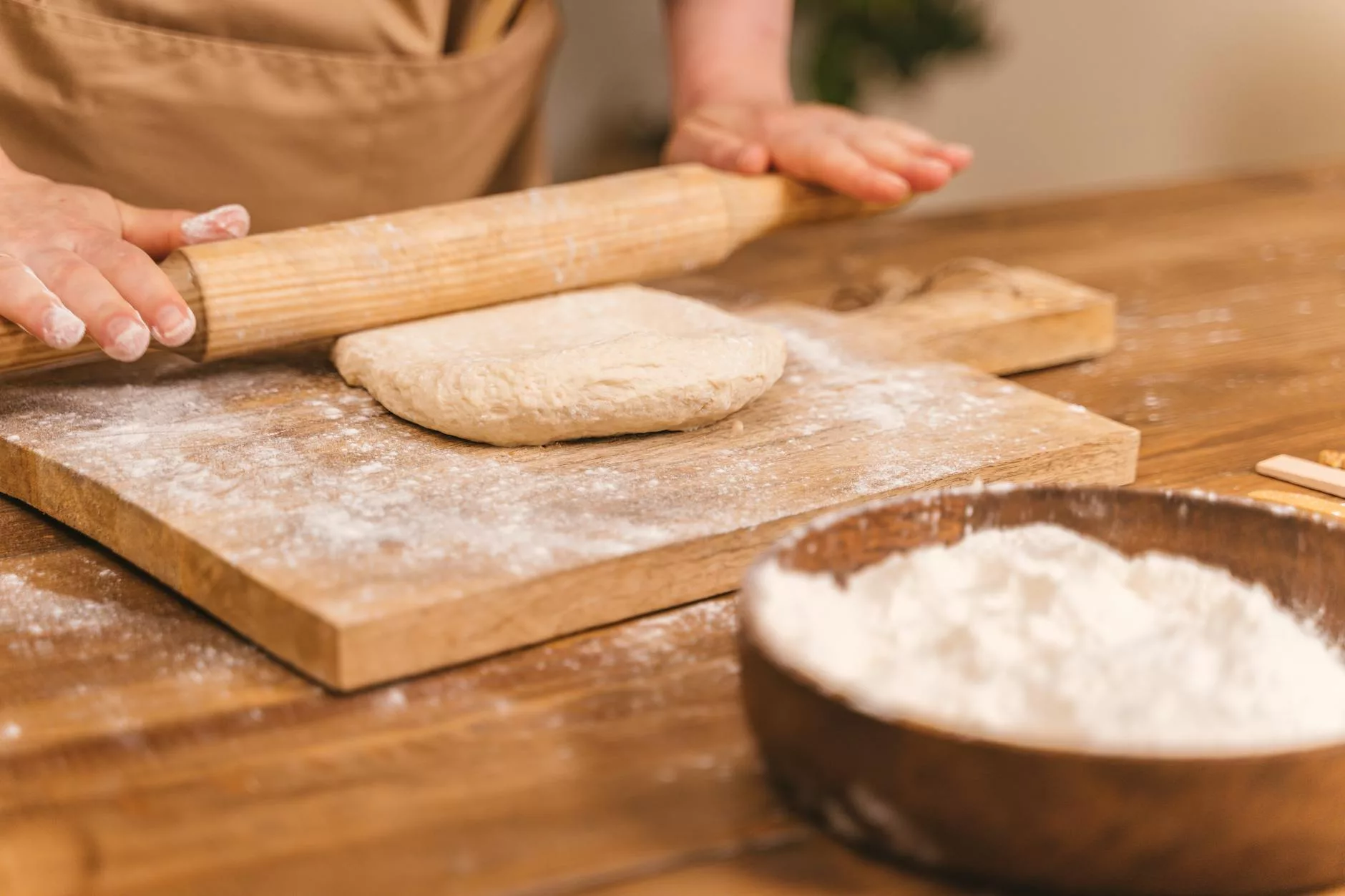 person kneading a dough with a wooden rolling pin